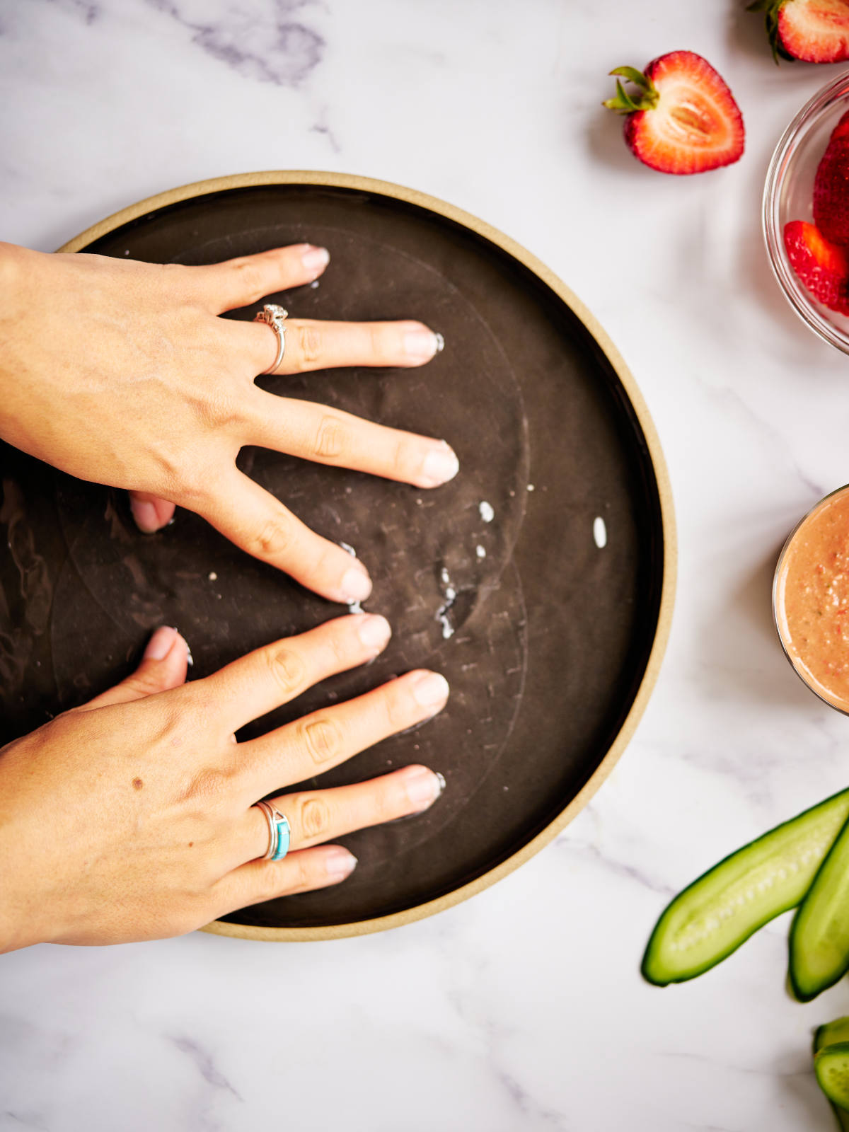 Two hands soaking rice paper sheets in a black dish with water.