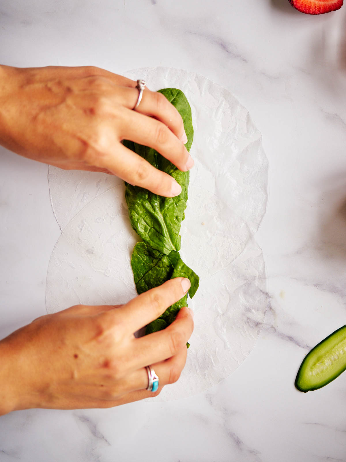 Two hands putting spinach on top of soaked rice paper.