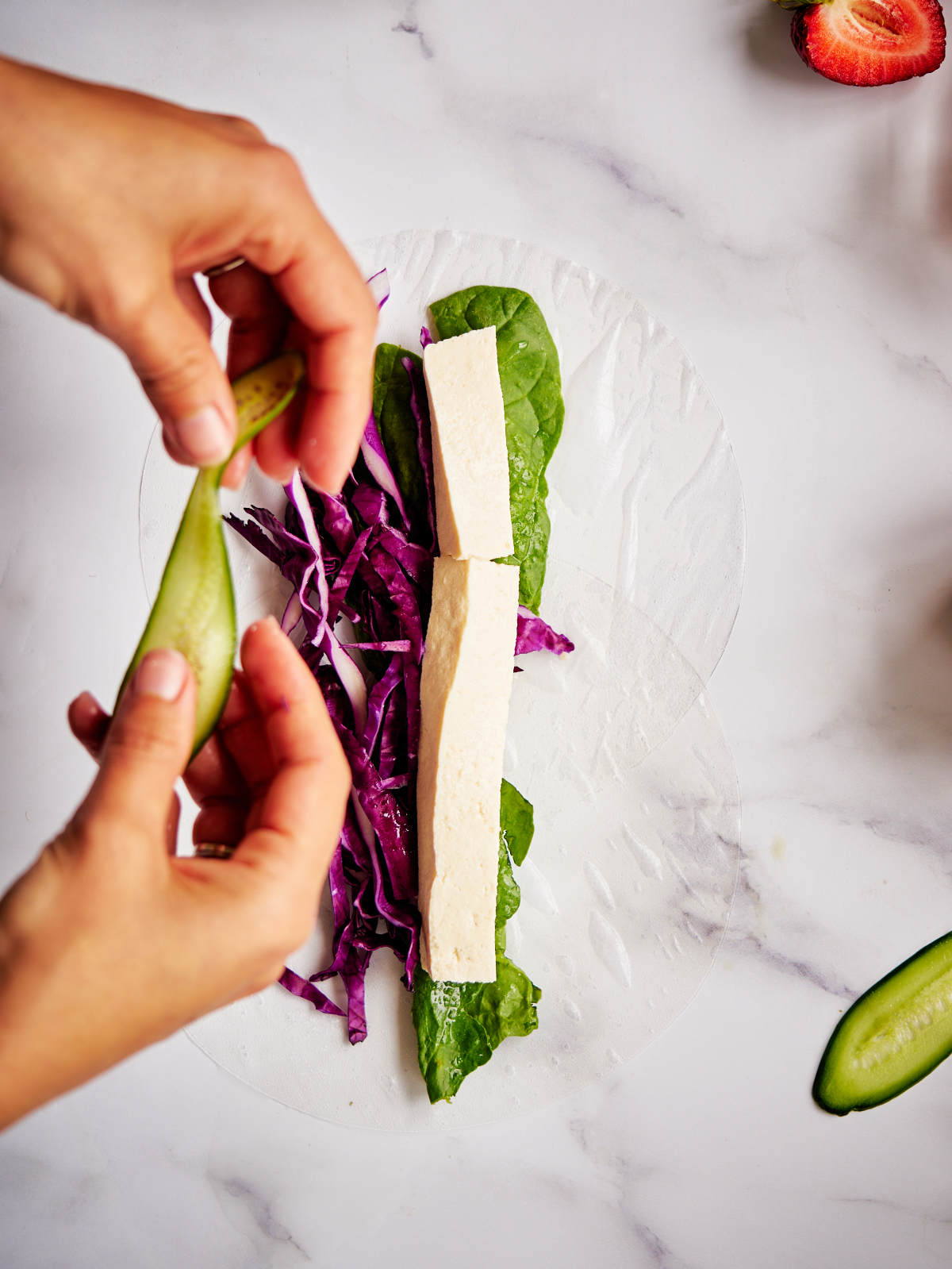 Two hands adding sliced cucumber to a salad roll.