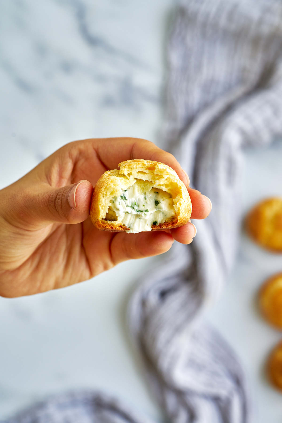 Hand holding a cream puff with a bite taken out.