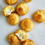 Cream puffs on a countertop with two cut open so you can see inside.