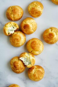 Cream puffs on a countertop with two cut open so you can see inside.