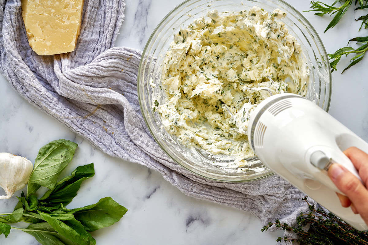 Whipping cream, cheese, and herbs in a glass mixing bowl.