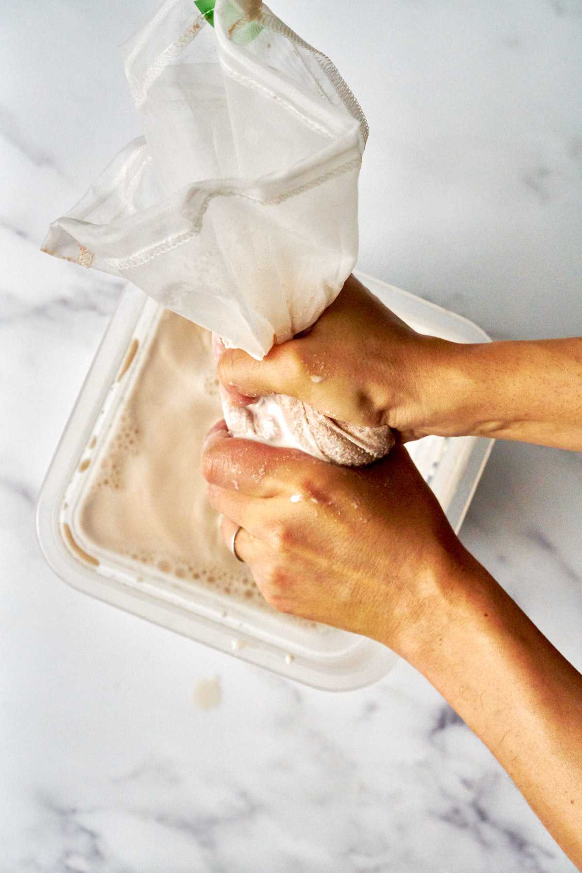 Squeezing nut milk into a square bowl.
