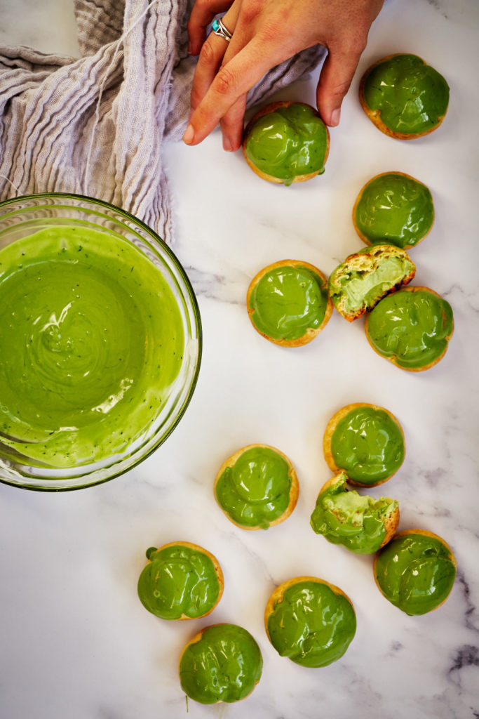 Green cream puffs with matcha next to a bowl of matcha chocolate.
