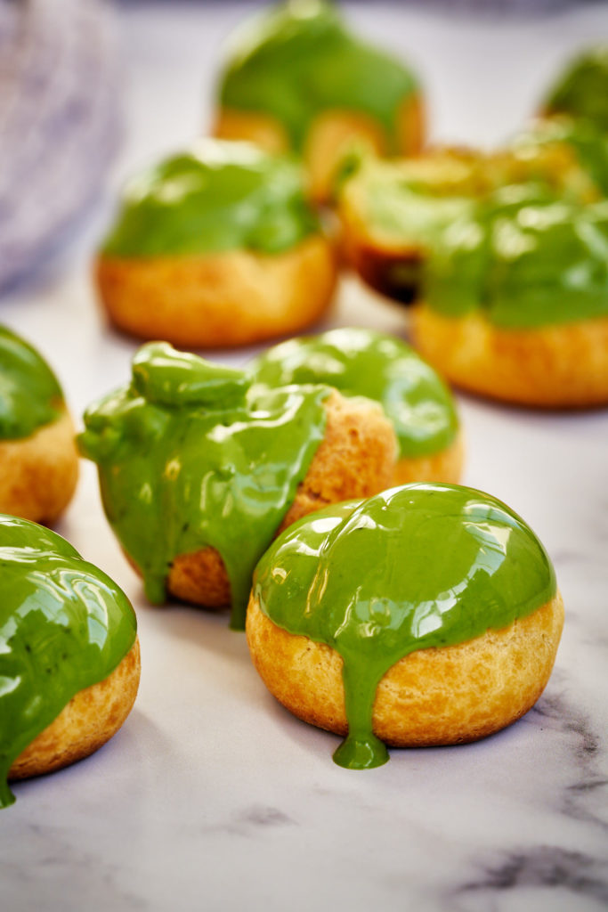 Cream puffs with green matcha chocolate shell.