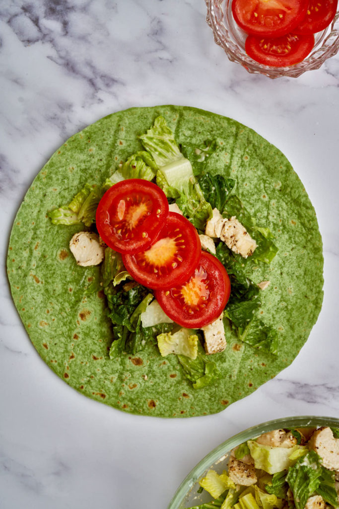 Open spinach wrap with salad, chicken, and tomatoes.
