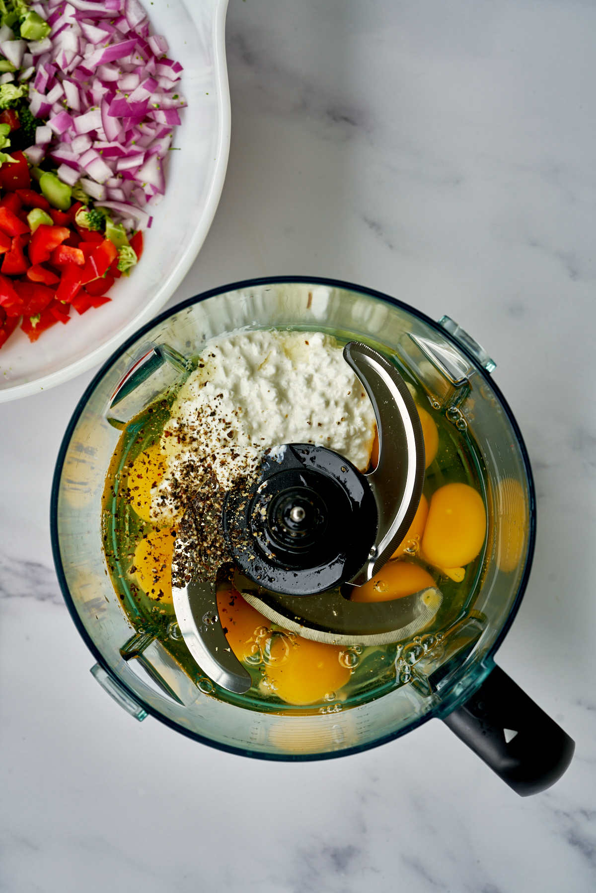 Eggs in a blender next to chopped vegetables.