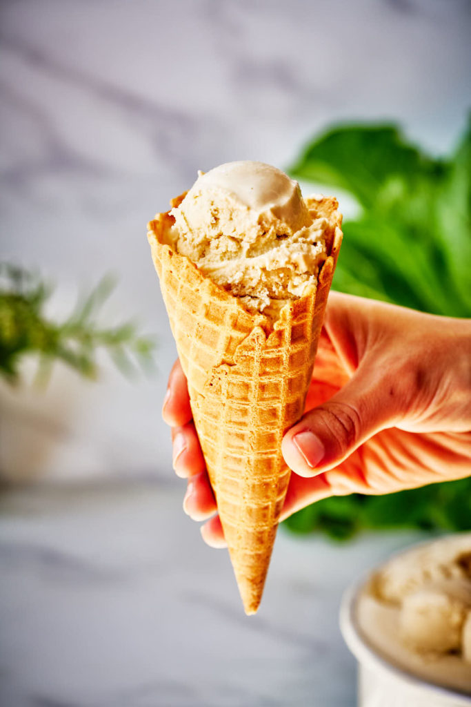 Hand holding ice cream cone with one scoop.