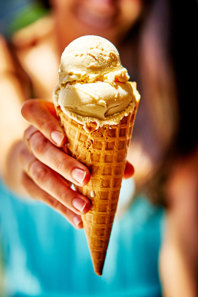 Hand holding ice cream cone with two scoops and girl in background.