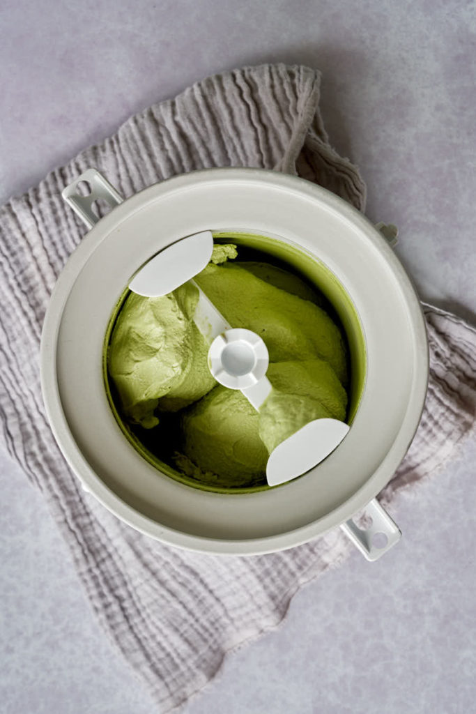 Green ice cream in KitchenAid ice cream attachment on grey background.