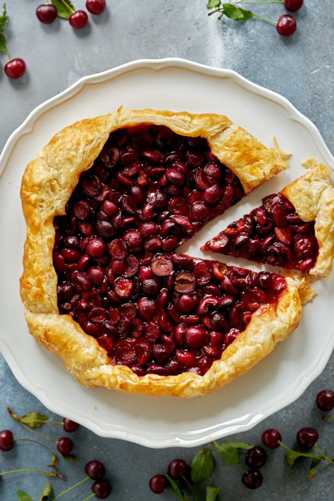 Cherry galette with a slice cut out on a white cake stand.