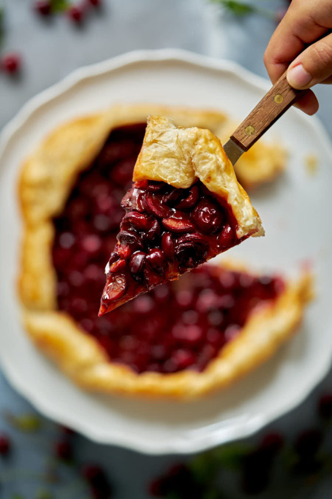 One slice of cherry galette held on a knife in a hand.