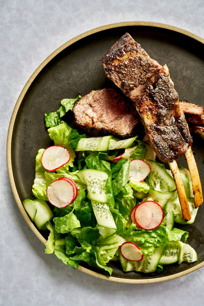 Rack of lamb with salad on a black plate.