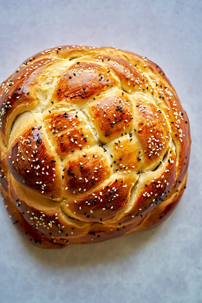 Round challah with sesame seeds flatlay on grey backdrop.