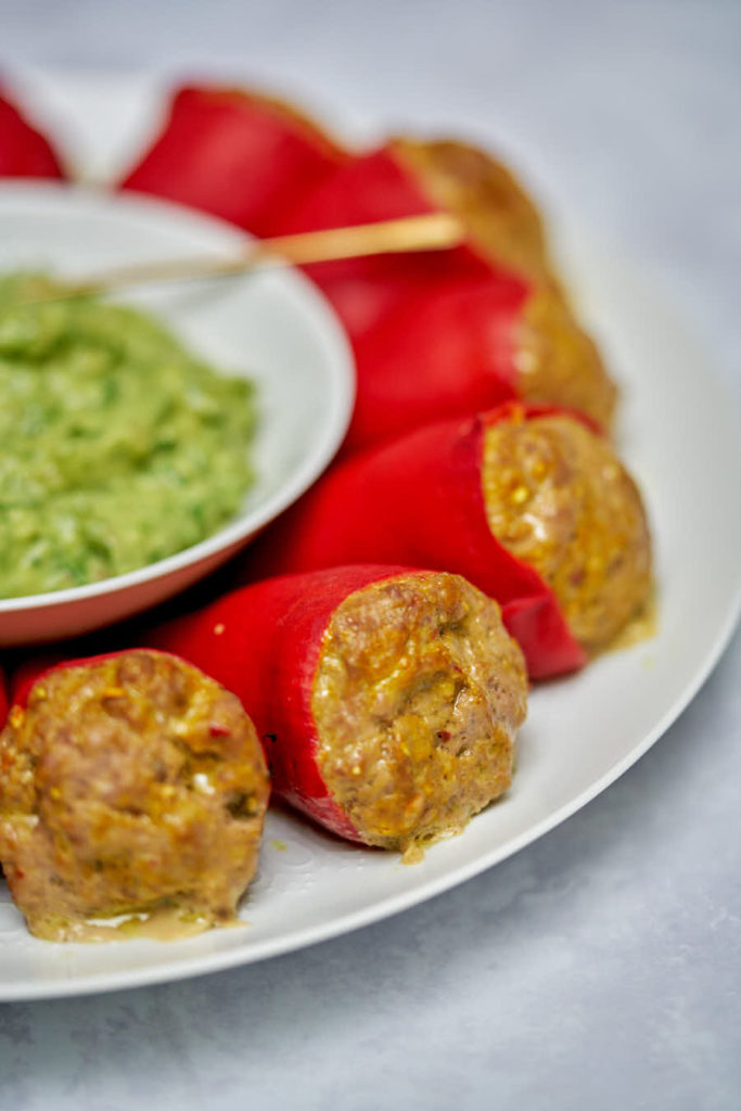 Stuffed red peppers on a white plate with green dipping sauce in the middle.