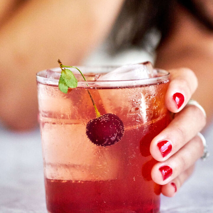 Girl with red nails holding glass with red cocktail.