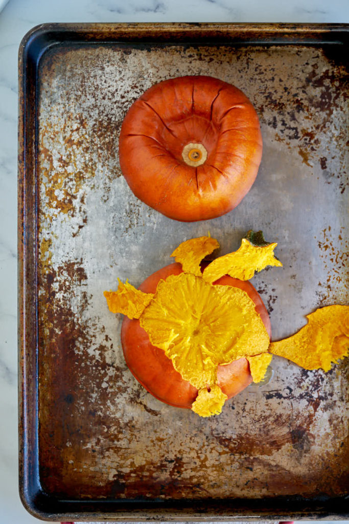 Peeled pumpkin cut in half on baking sheet.