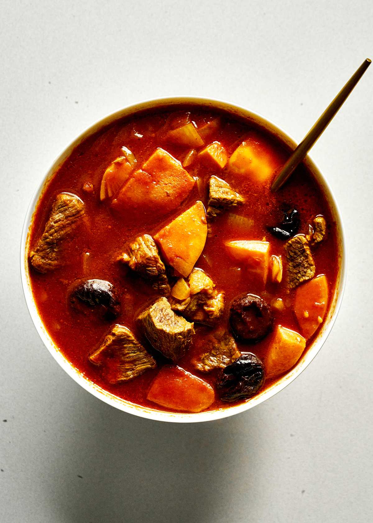 Red stew in white dish on black table.