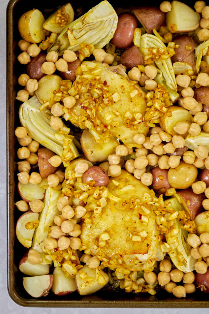 Dark baking tray with red potatoes, chicken, and fennel.