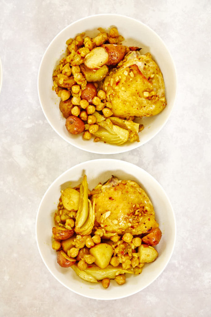 Two white bowls with yellow chicken, chickpeas, and potatoes.