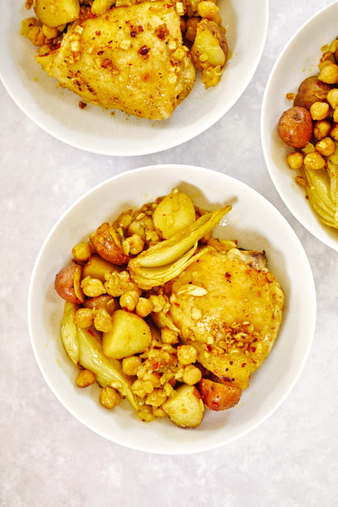 Bowls with chicken, chickpeas, and fennel on a grey backdrop.
