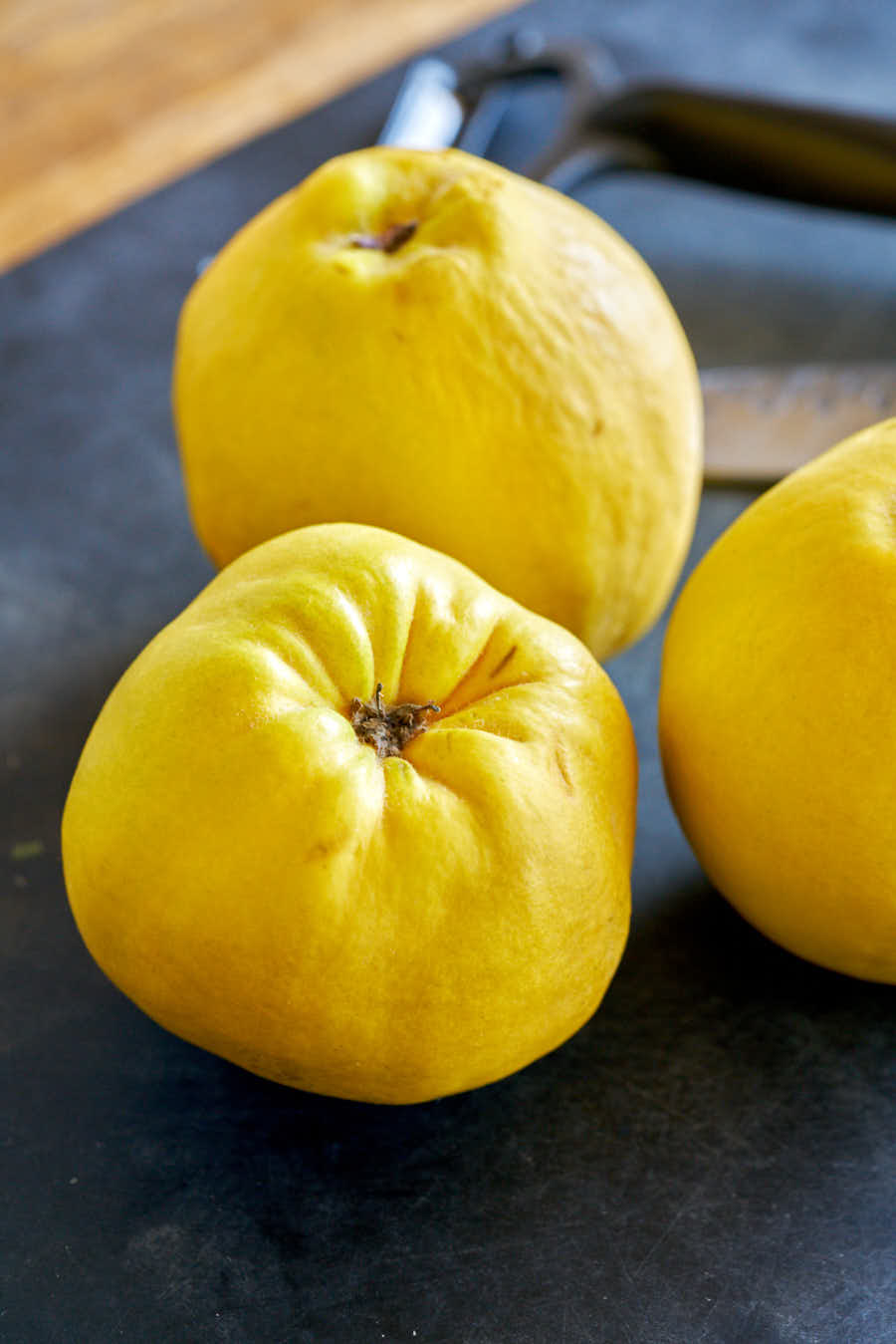 Three yellow quince on black cutting board.