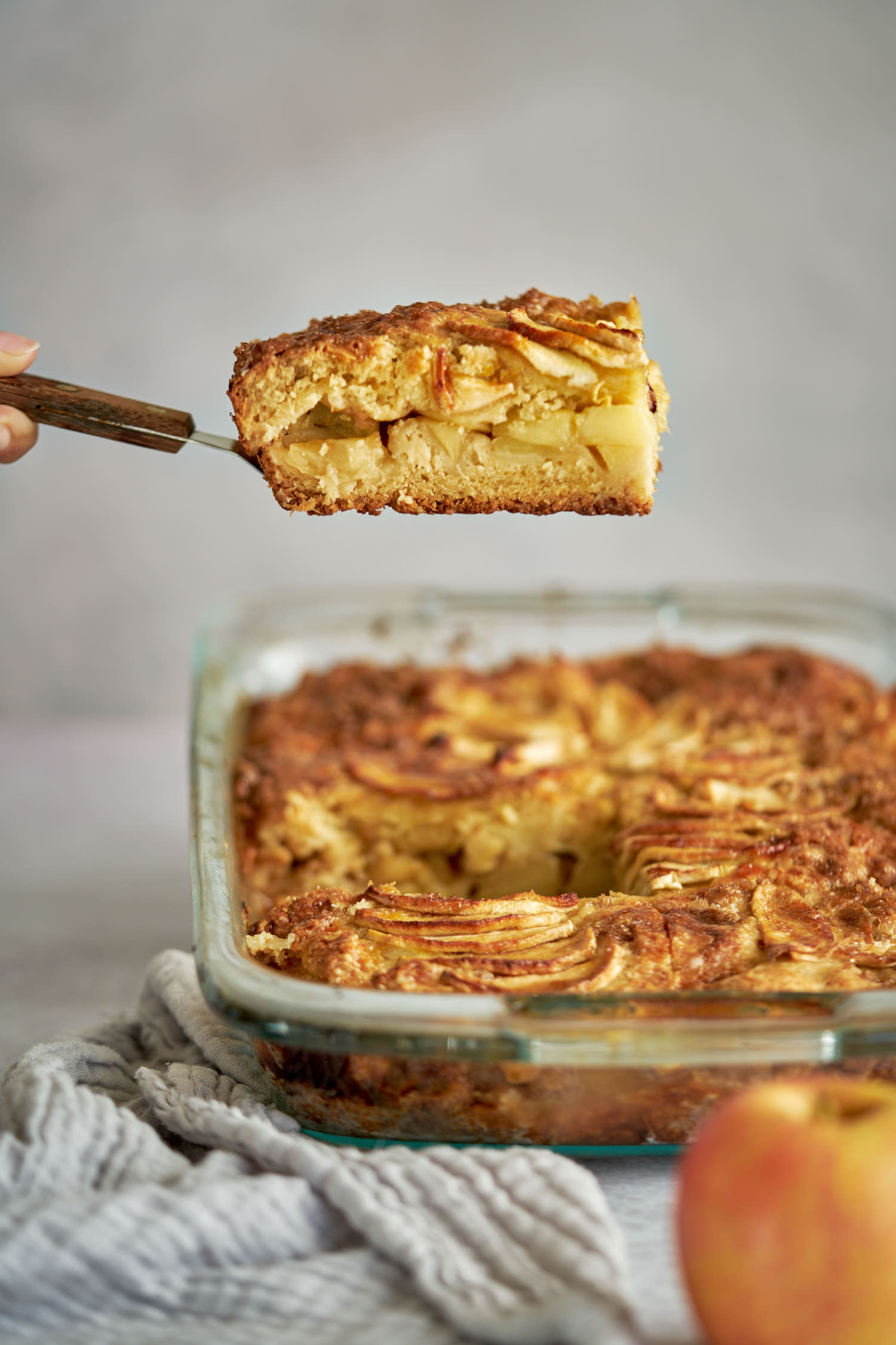 Sliced apple cake on a spatula over a whole cake.