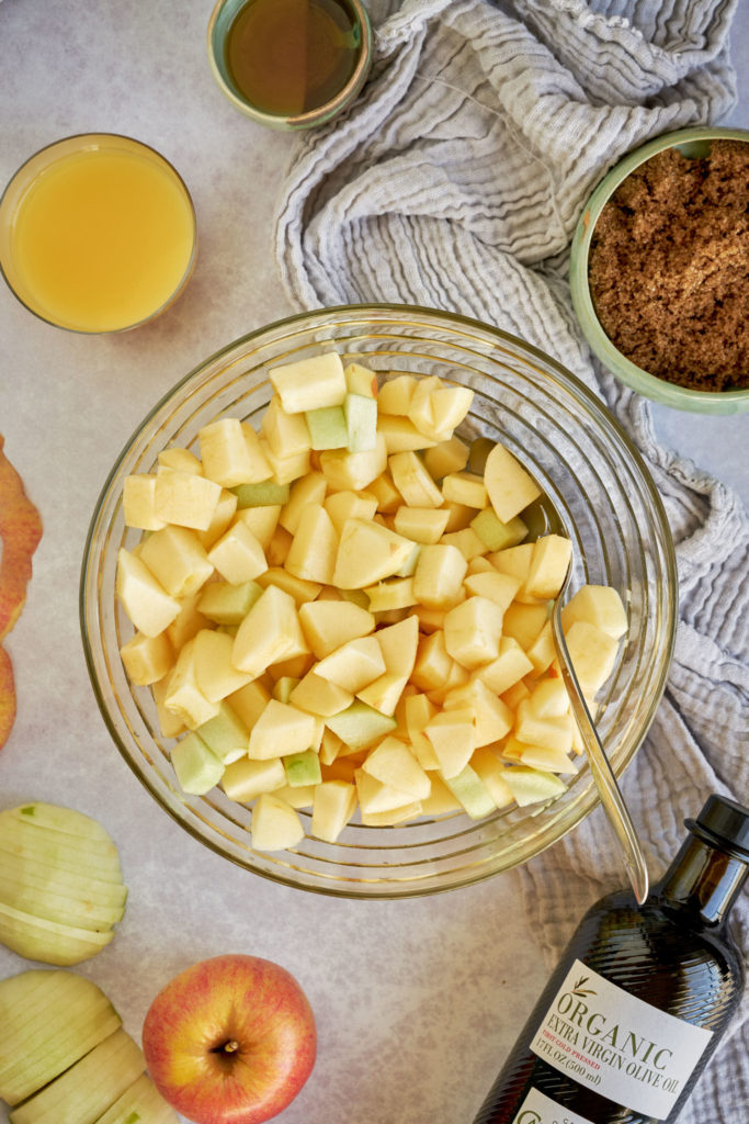 Chopped apples in a mixing bowl surrounded by ingredients.
