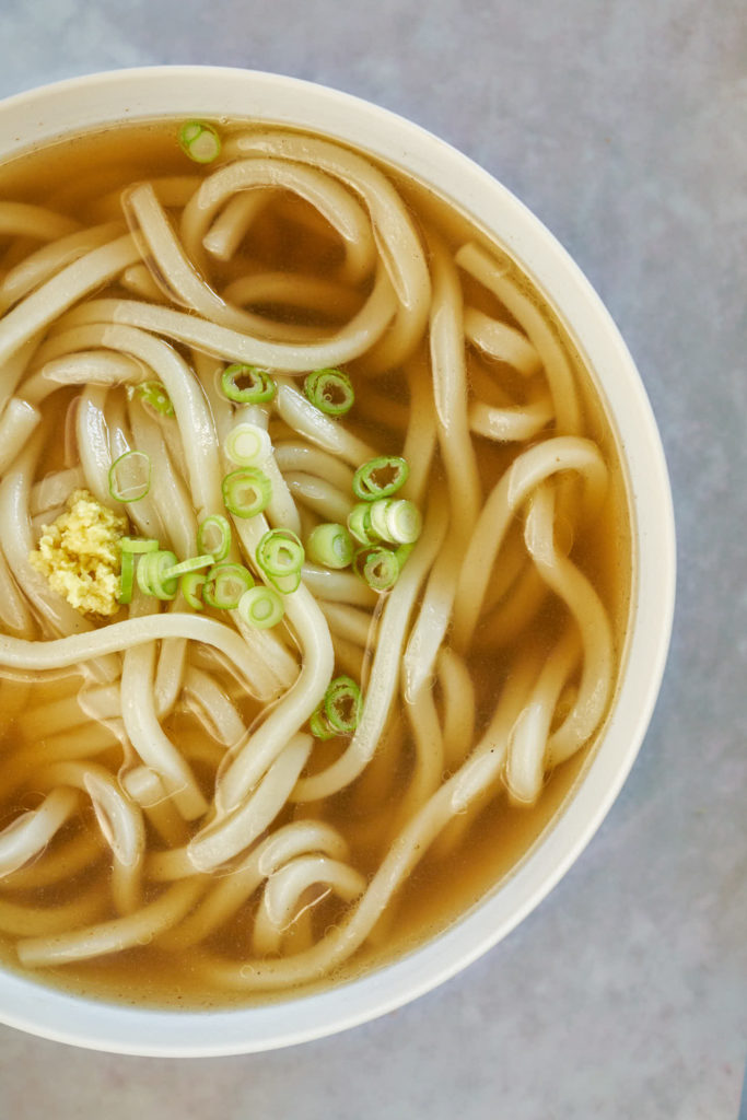 White bowl with udon noodles and soup.