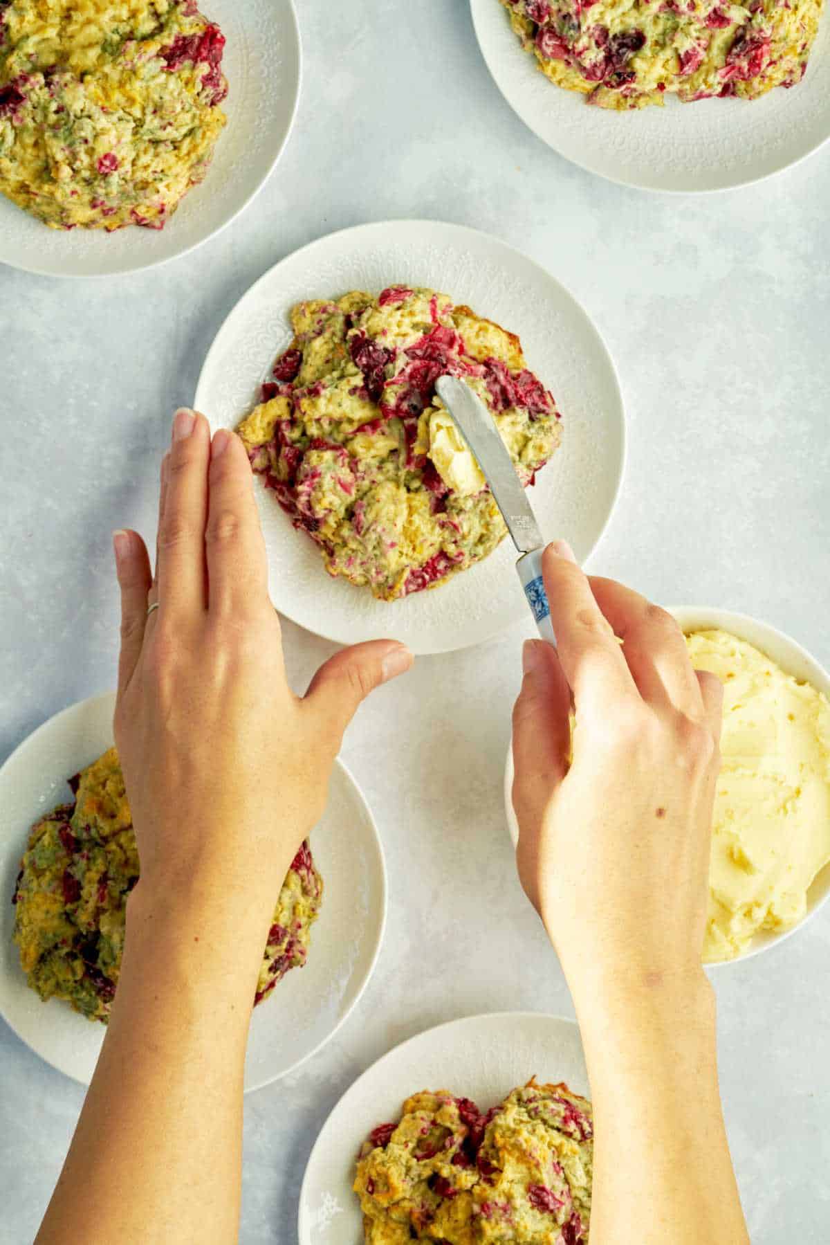 Hands spreading butter on a scone.