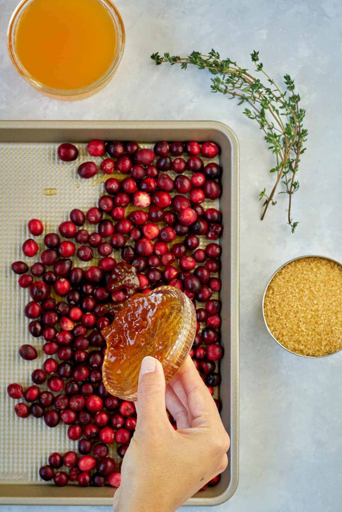 Pouring honey over cranberries in a sheet pan.