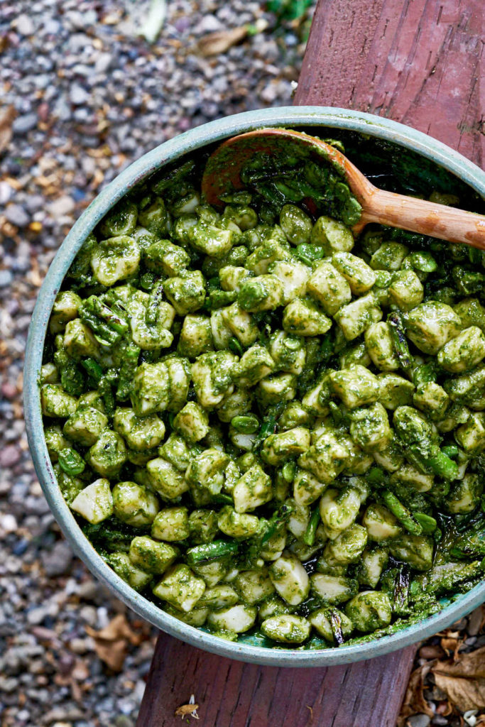 Gnocchi with pesto and other green vegetables in a blue ceramic bowl on a wood plank.