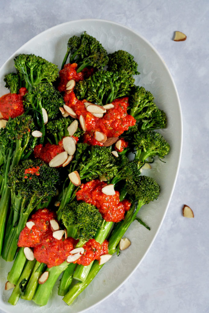 Roasted broccoli with red sauce and almonds on white plate.