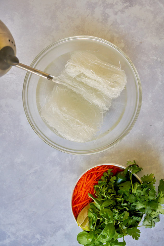 Pouring hot water from a kettle over white noodles.