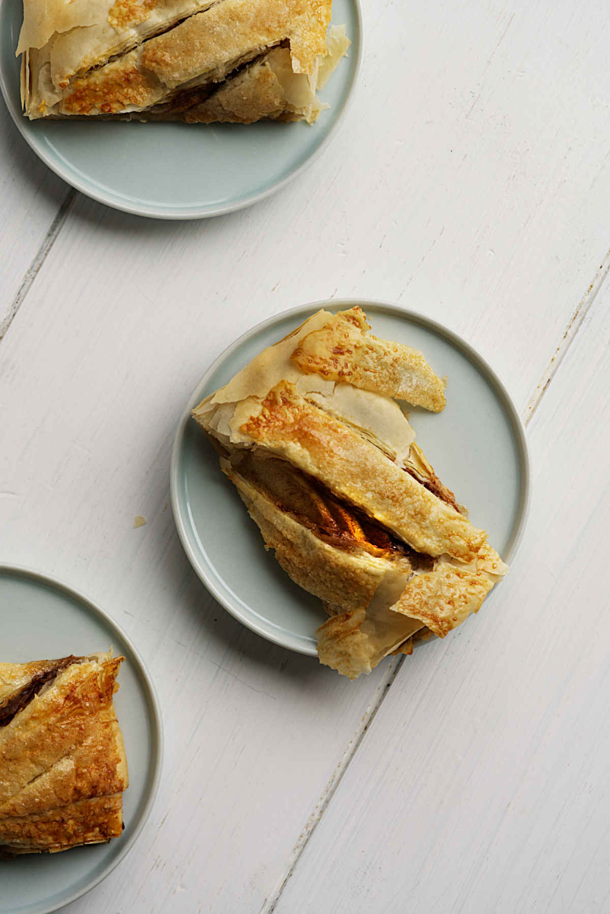 Apple strudel slices on individual light green plates on a white wooden backdrop.