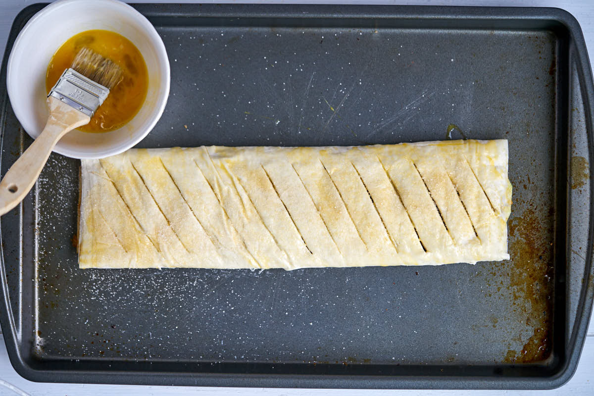 Raw pastry on a baking sheet next to egg wash.