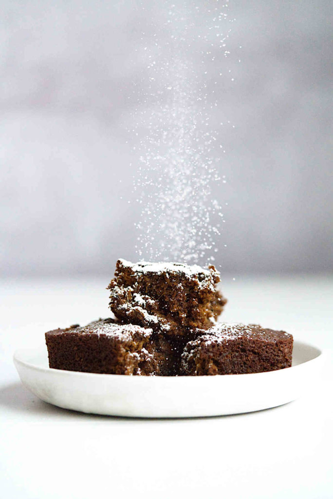 Sprinkling powdered sugar on cake on a white plate.