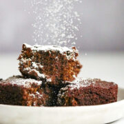 Brown cake being sprinkled with powdered sugar.