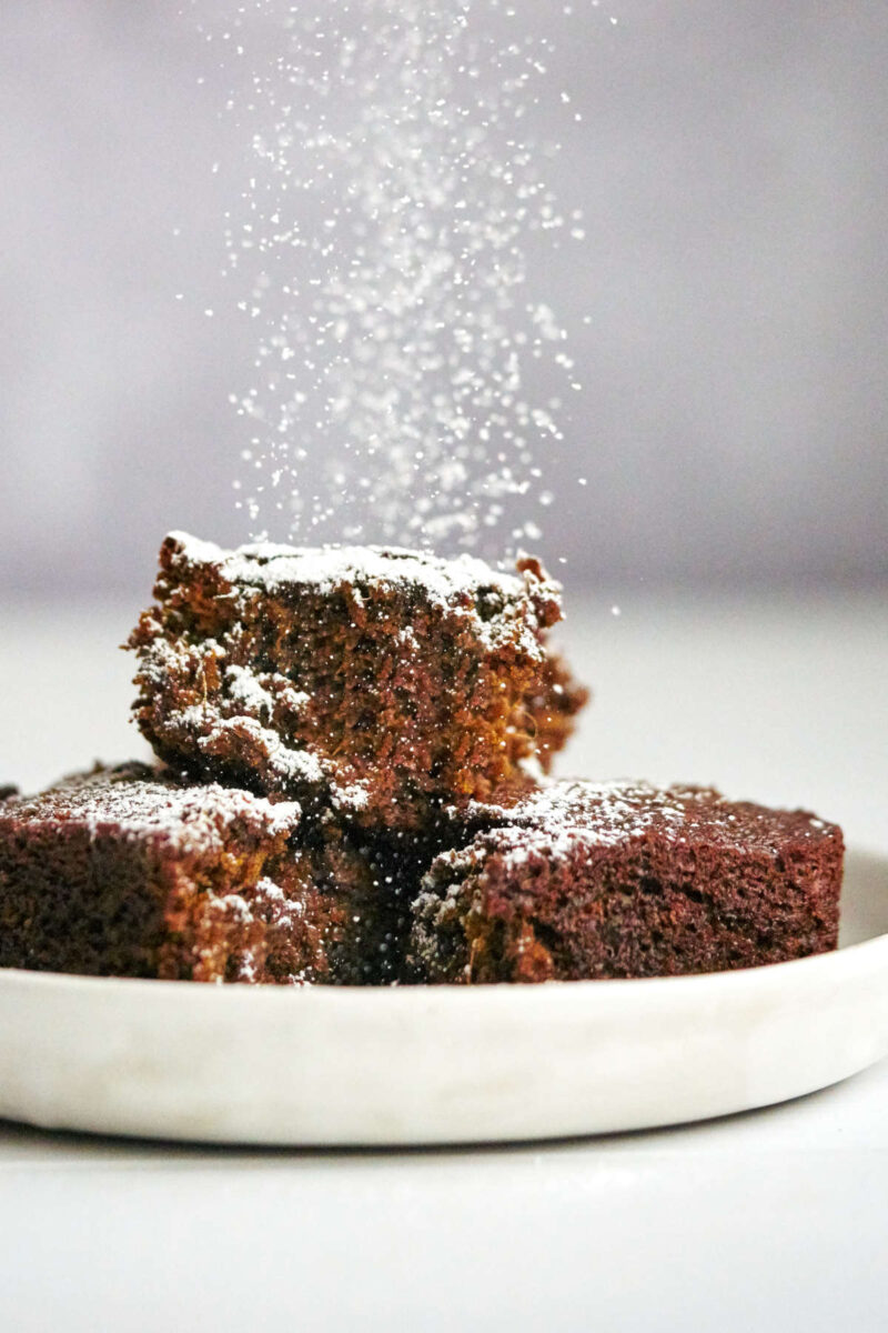 Brown cake being sprinkled with powdered sugar.