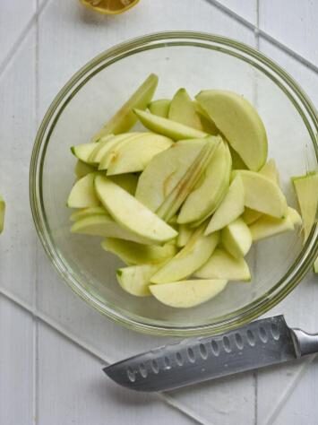 Slices of apples in a glass bowl next to a knife.