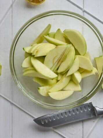 Slices of green apples in a glass bowl next to a knife.