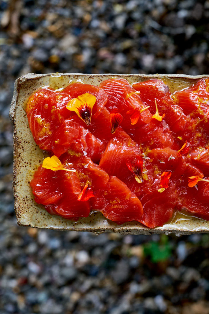 Salmon crudo on a ceramic platter decorated with nasturtium petals.