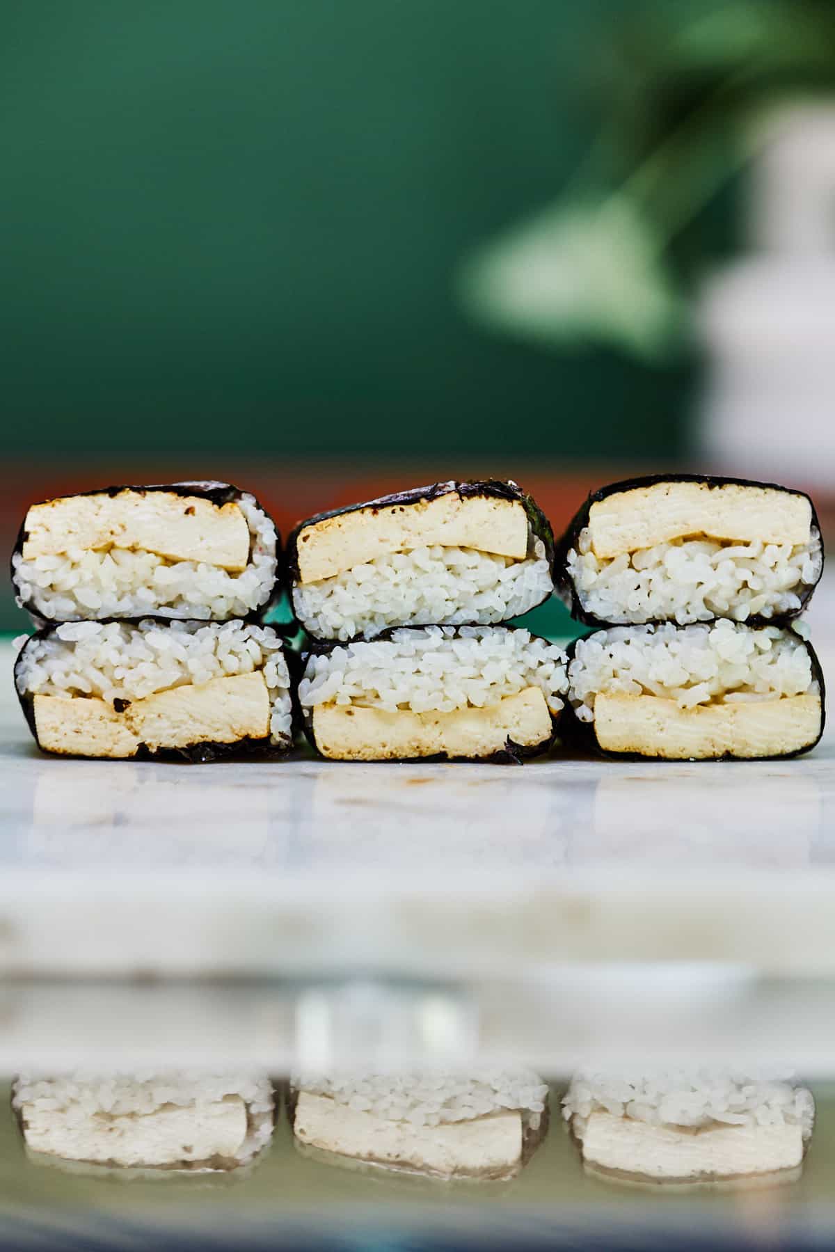 Six tofu musubi stacked on a white countertop.