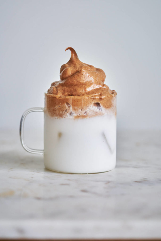 Whipped chocolate over milk in a clear glass cup.