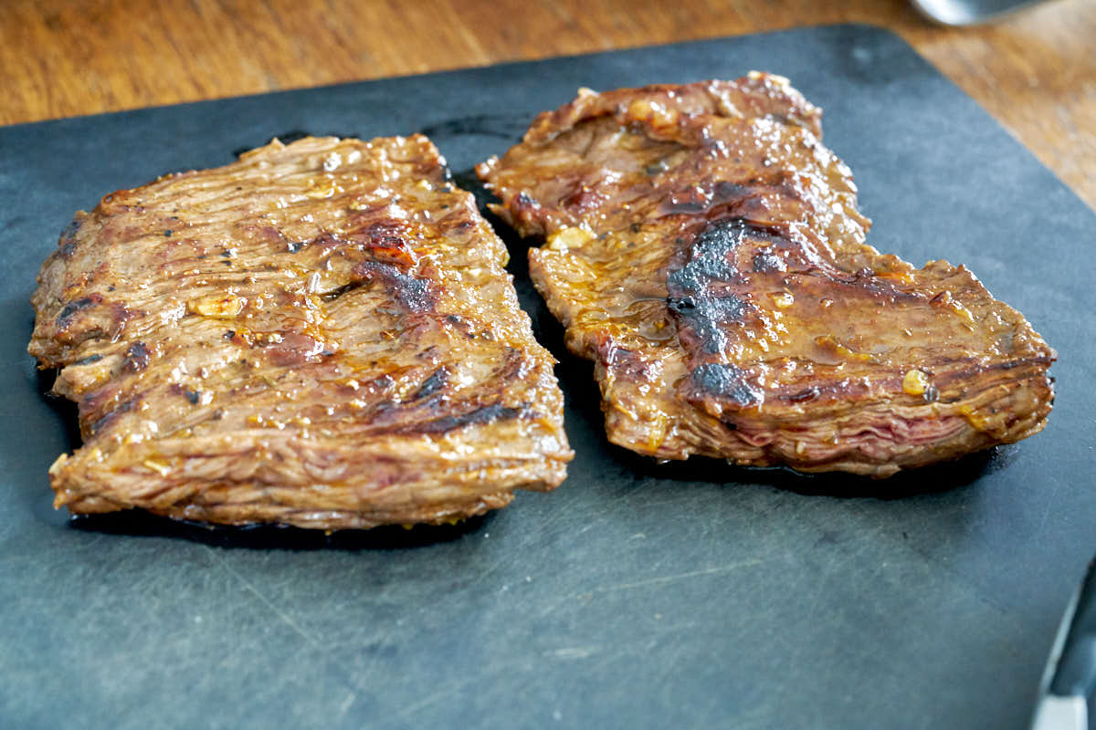 Cooked skirt steak on a black cutting board.