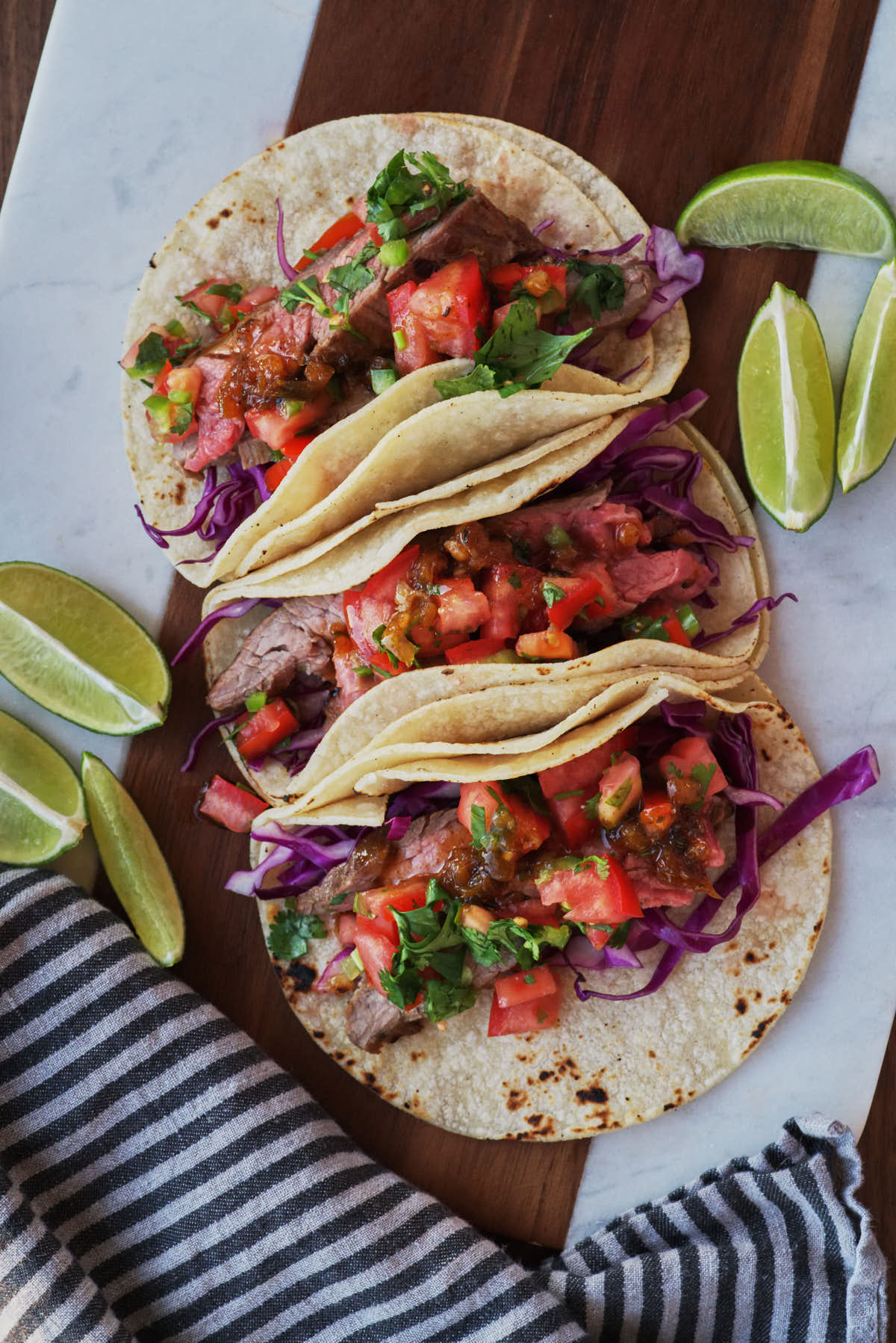 Three steak tacos on a cutting board with sliced limes.