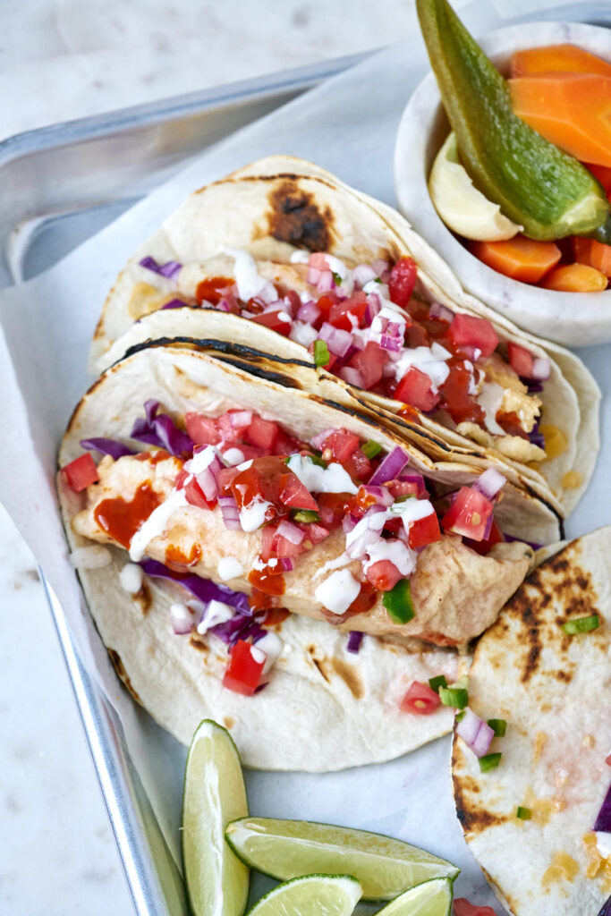 Top view of fish tacos with salsa, escabeche, and limes.