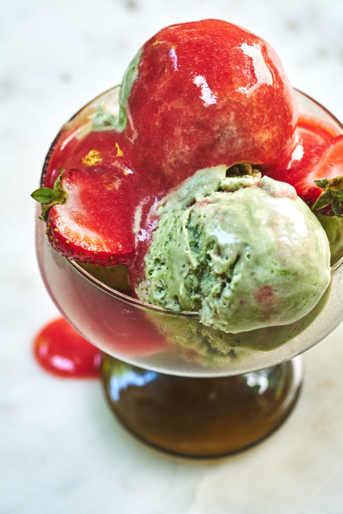 Pedestal glass with strawberry matcha semifreddo scoops, strawberries, and strawberry sauce.