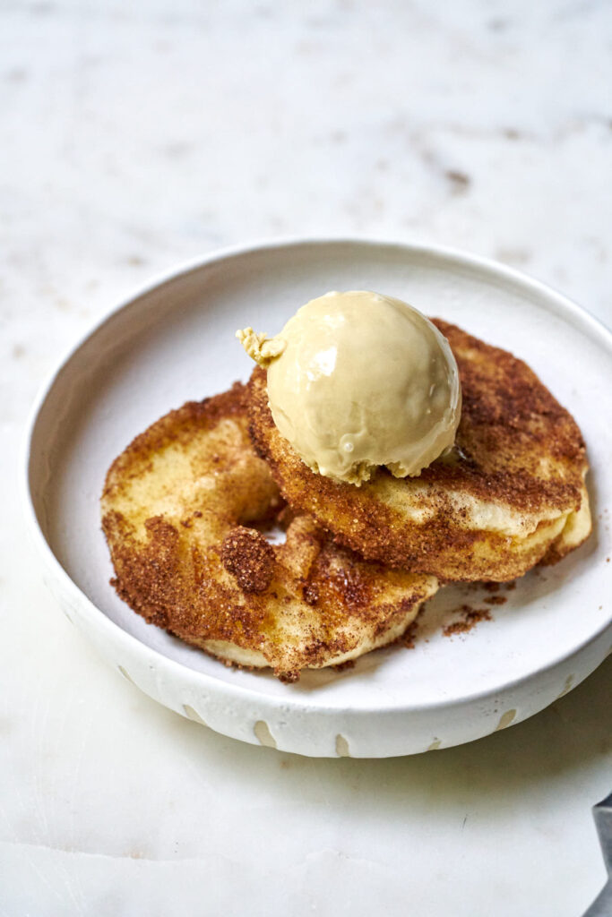 Two slices of fried apple topped with a scoop of ice cream on a white plate.